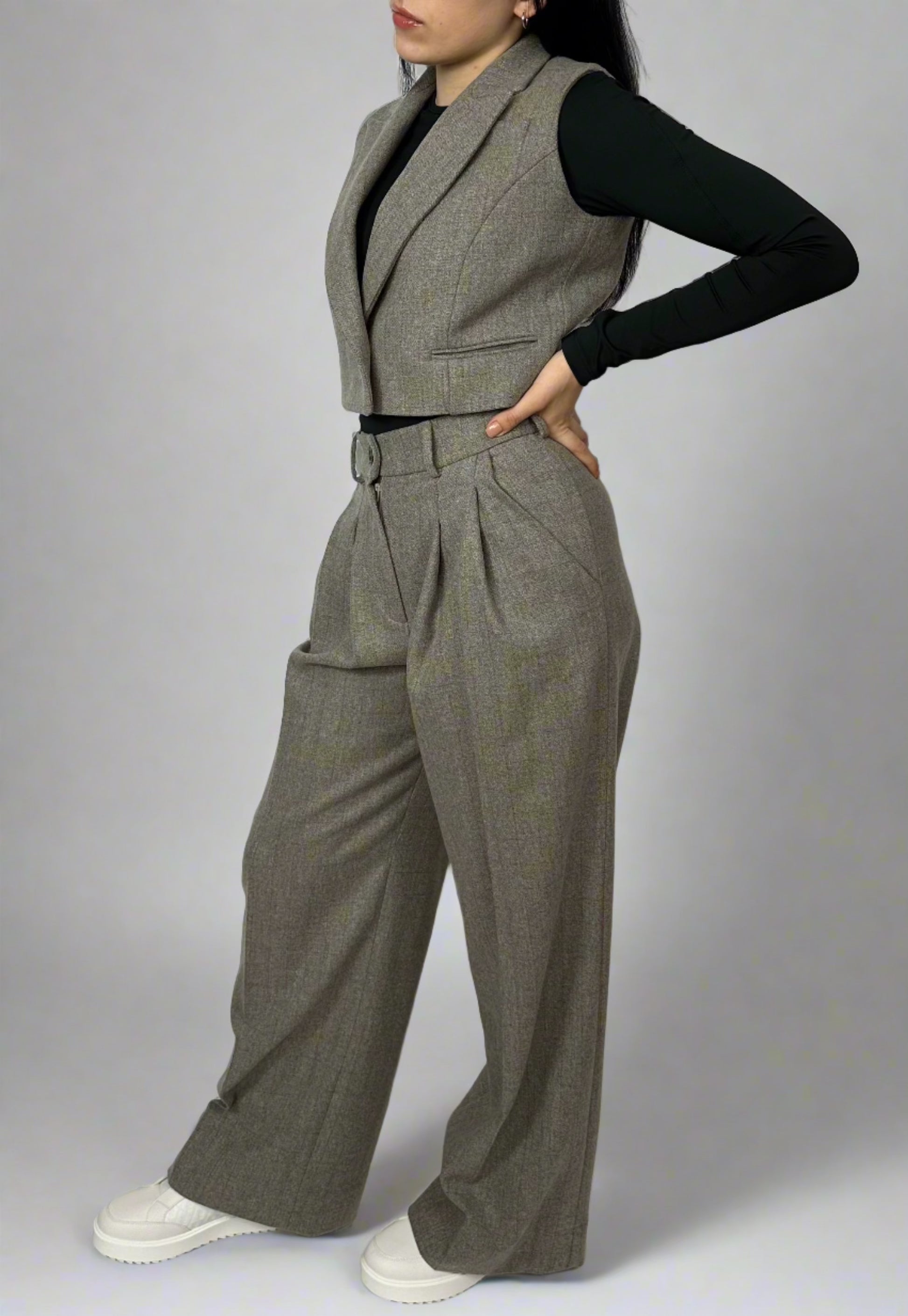 Model showcasing Sartorial Flair grey waistcoat and high-waisted trousers. The single-button waistcoat is paired with a black long-sleeve top and white trainers, emphasizing a smart casual look. The outfit highlights the versatility of suits, suitable for both formal and casual settings.