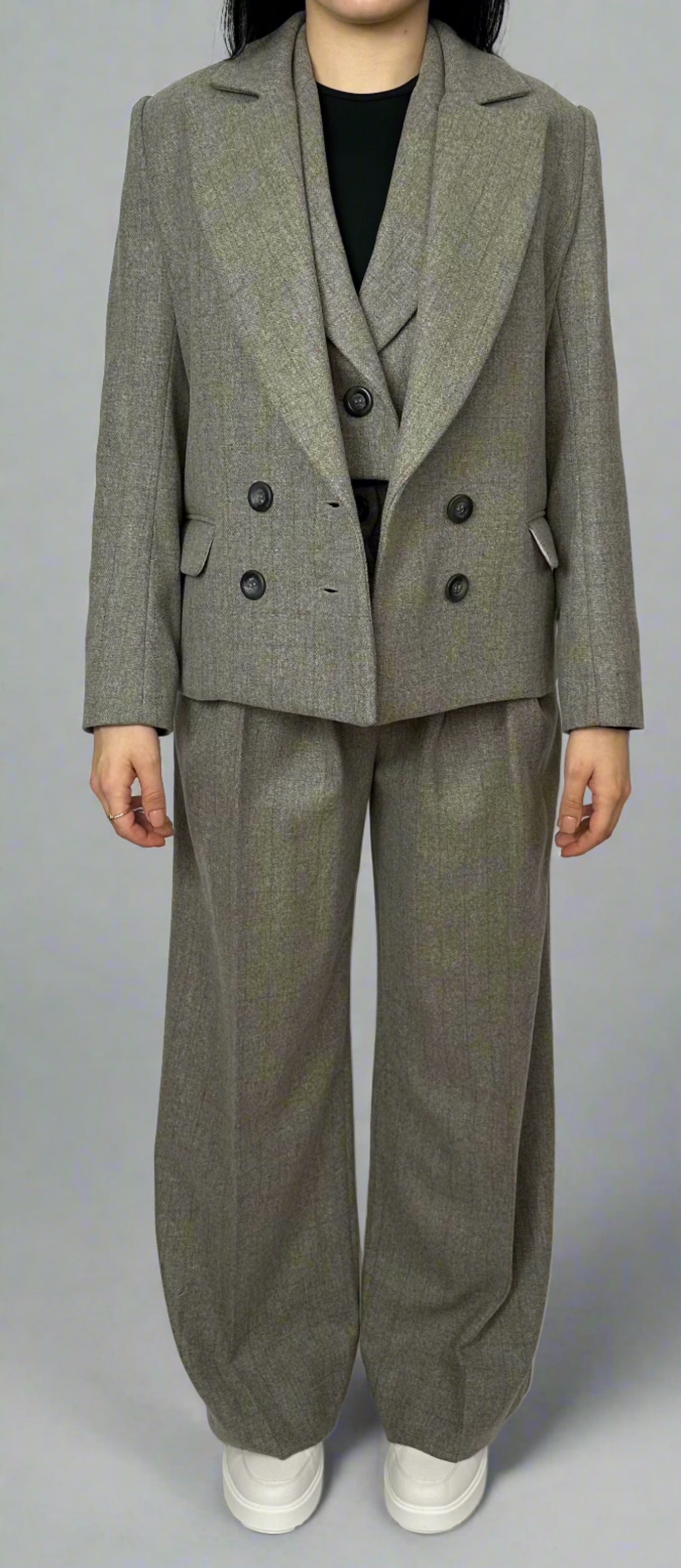 Front view of a model wearing a Sartorial Flair grey three-piece suit, including a double-breasted blazer, waistcoat, and matching trousers. The outfit is paired with white trainers for a smart casual look, demonstrating the versatility of the suit for both formal and casual occasions.