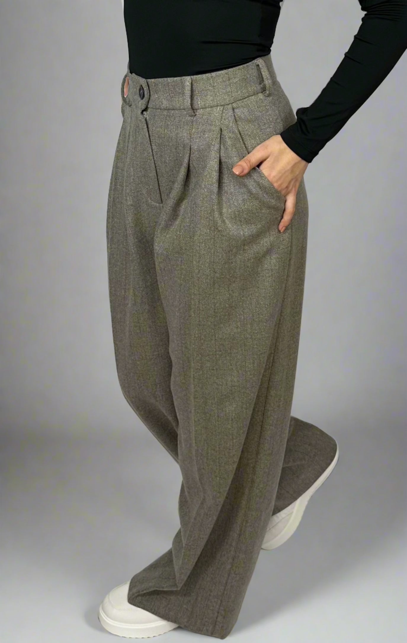 Side view of a model showcasing Sartorial Flair grey high-waisted trousers, paired with a black top and white trainers. The pleated design and relaxed fit highlight the versatility of the trousers, suitable for both formal and smart casual looks