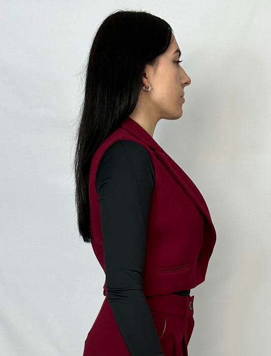 Side profile of model wearing Sartorial Flair burgundy waistcoat and wide-leg trousers, paired with a black top, highlighting the tailored fit and sophisticated design of the ensemble.