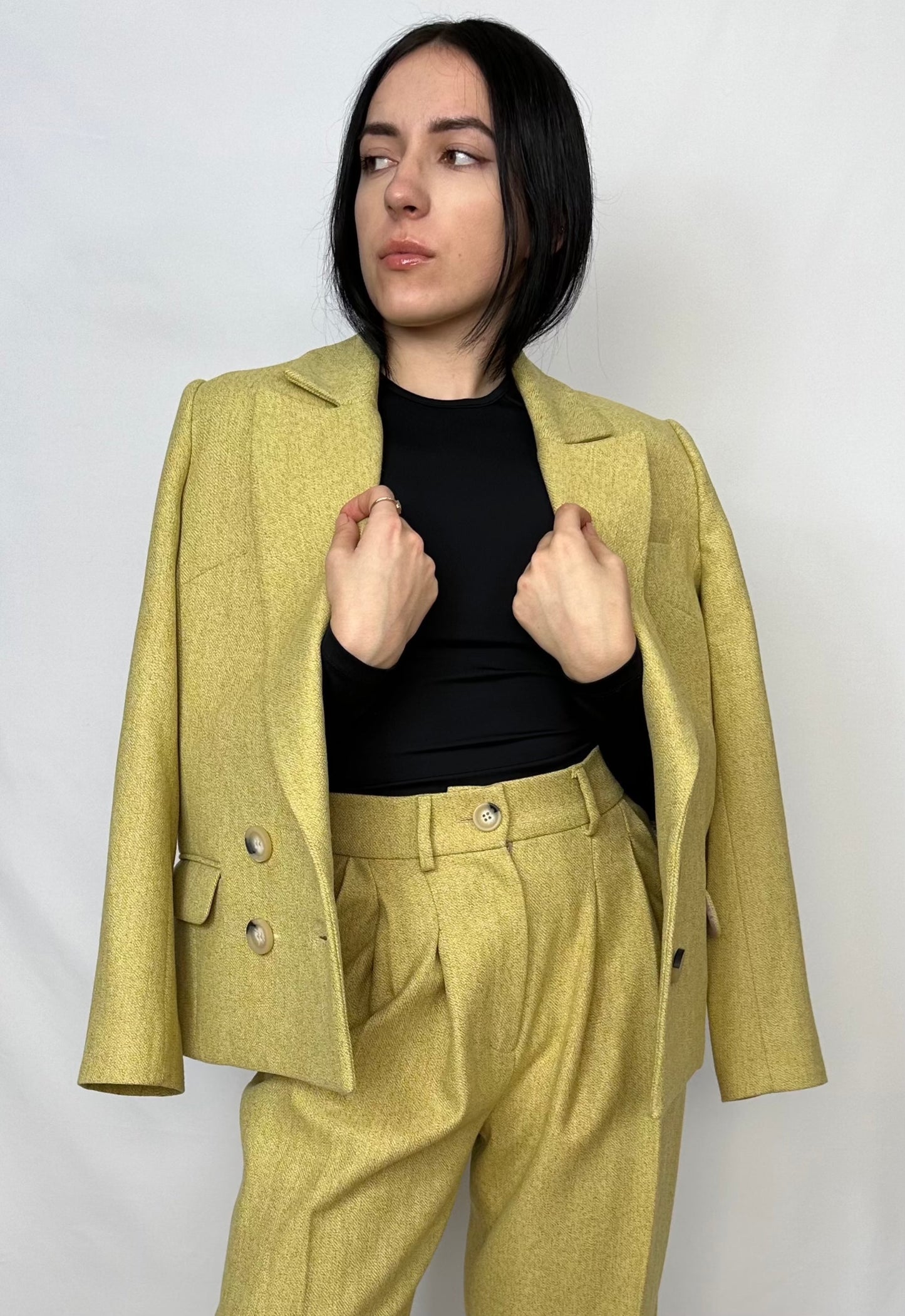 Confident woman modeling a chartreuse Sartorial Flair wool suit with a stylish double-breasted blazer and matching trousers, perfect for a bold and fashionable statement.