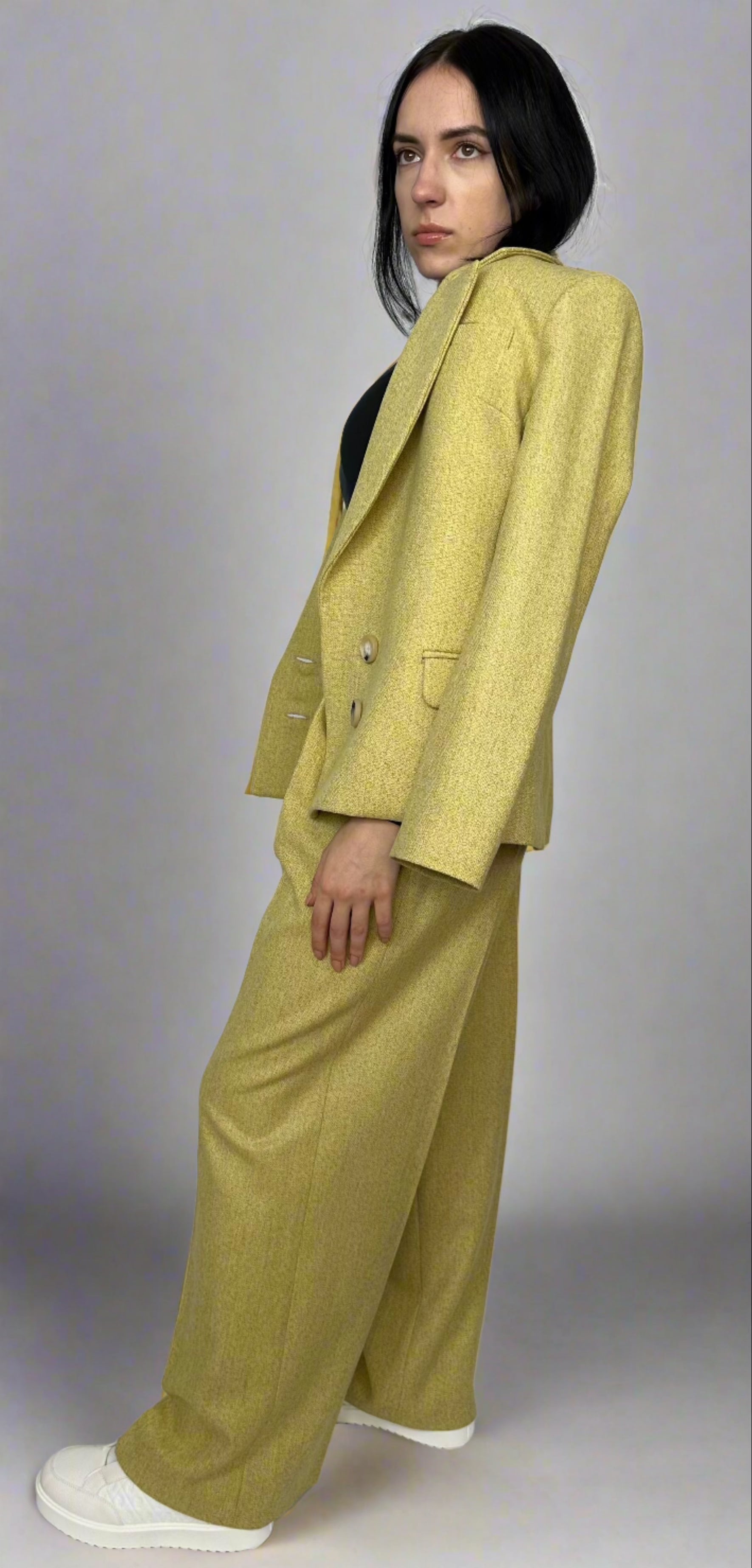 Side profile of a young woman in a textured chartreuse suit by Sartorial Flair, featuring a double-breasted blazer and wide-leg trousers, exuding elegance and contemporary style.