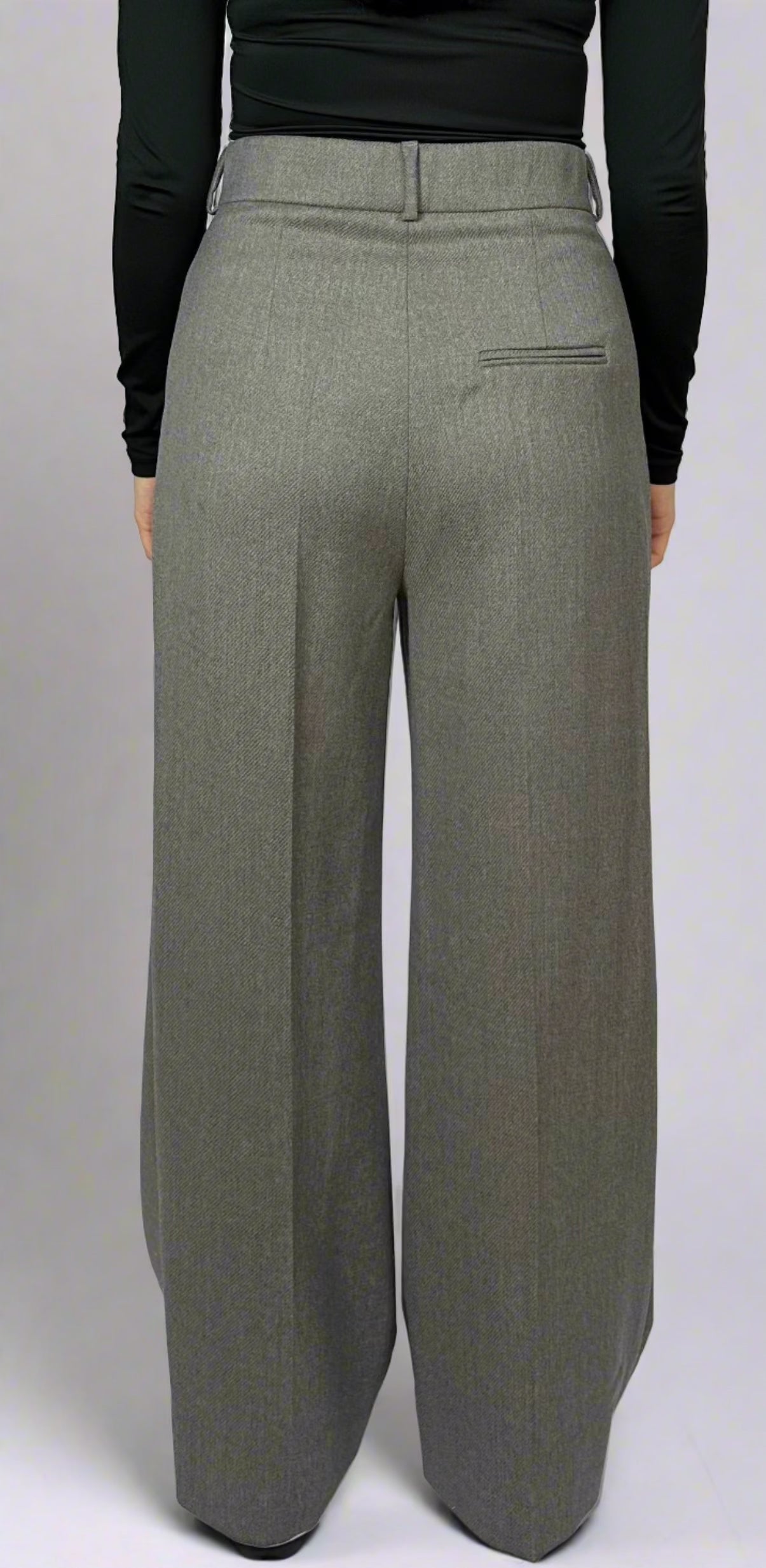 women's suit trousers in grey, backClose-up view of a woman modeling gray wide-leg trousers, featuring meticulous tailoring and pleated details.