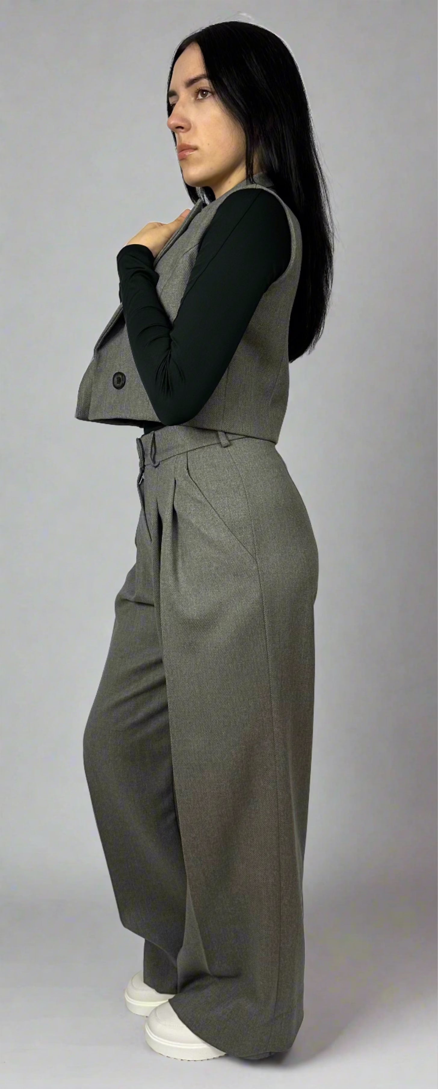 Side profile of a woman elegantly posing in a tailored Zoe gray waistcoat and matching wide-leg trousers, showcasing a sophisticated business outfit.