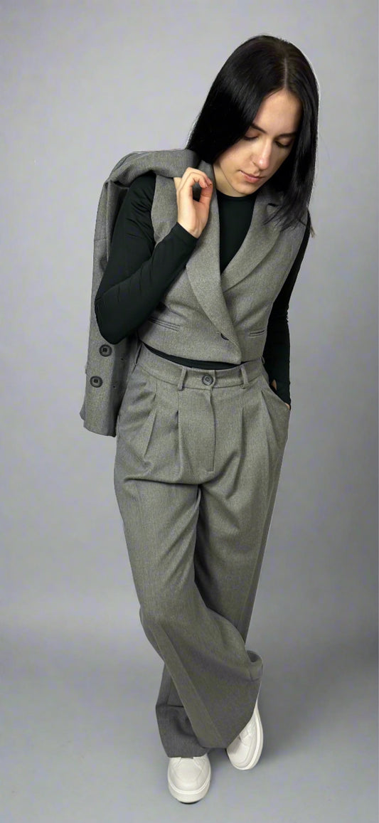 Elegant woman posing with Zoe gray suit vest over shoulder, complementing the formal high-waisted trousers and fitted black turtleneck, perfect for a sophisticated business look, available at Sartorial Flair.