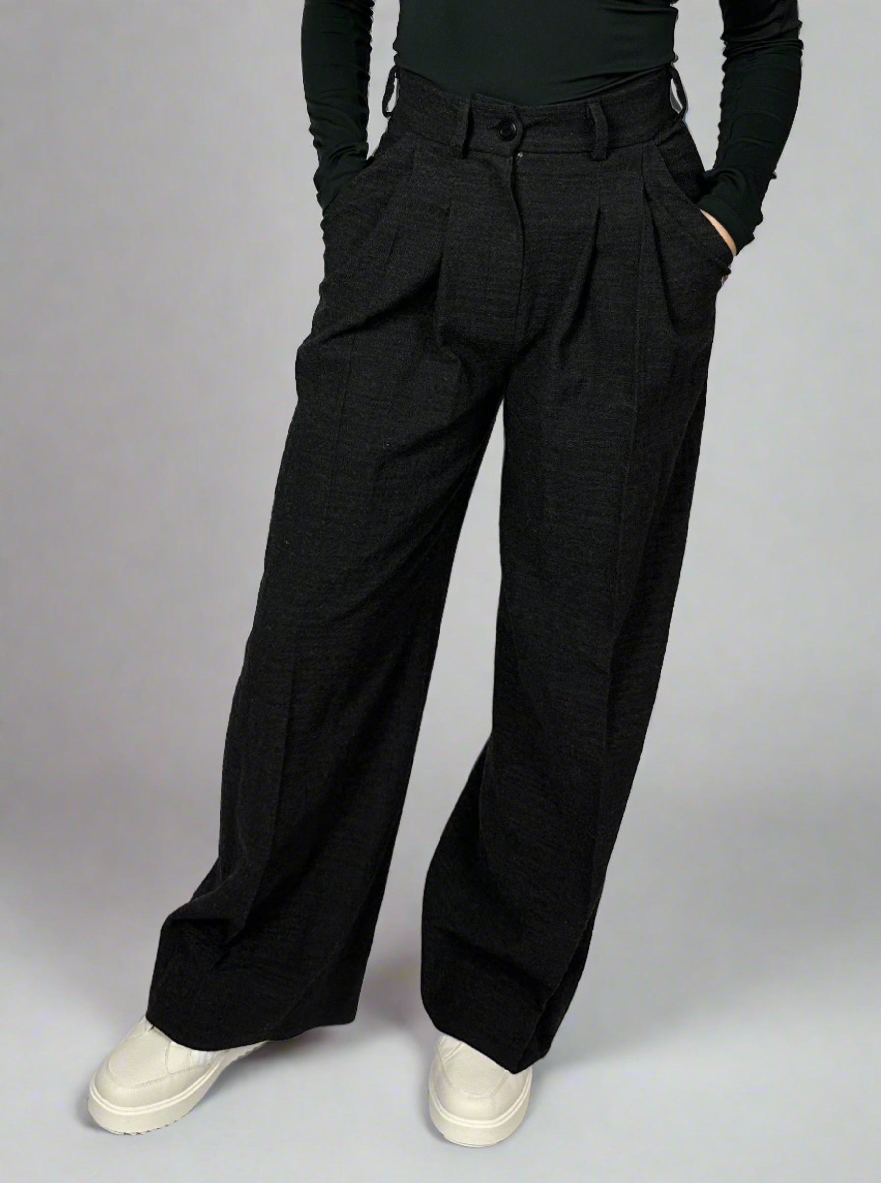 Front view of a model showcasing Sartorial Flair’s black wide-leg trousers, paired with white trainers for a smart casual look. The high-waisted trousers feature a pleated front and a relaxed, wide-leg design, ensuring both style and comfort. Sartorial Flair suits are not only suitable for formal wear but can also be styled for a smart casual look by pairing them with trainers.