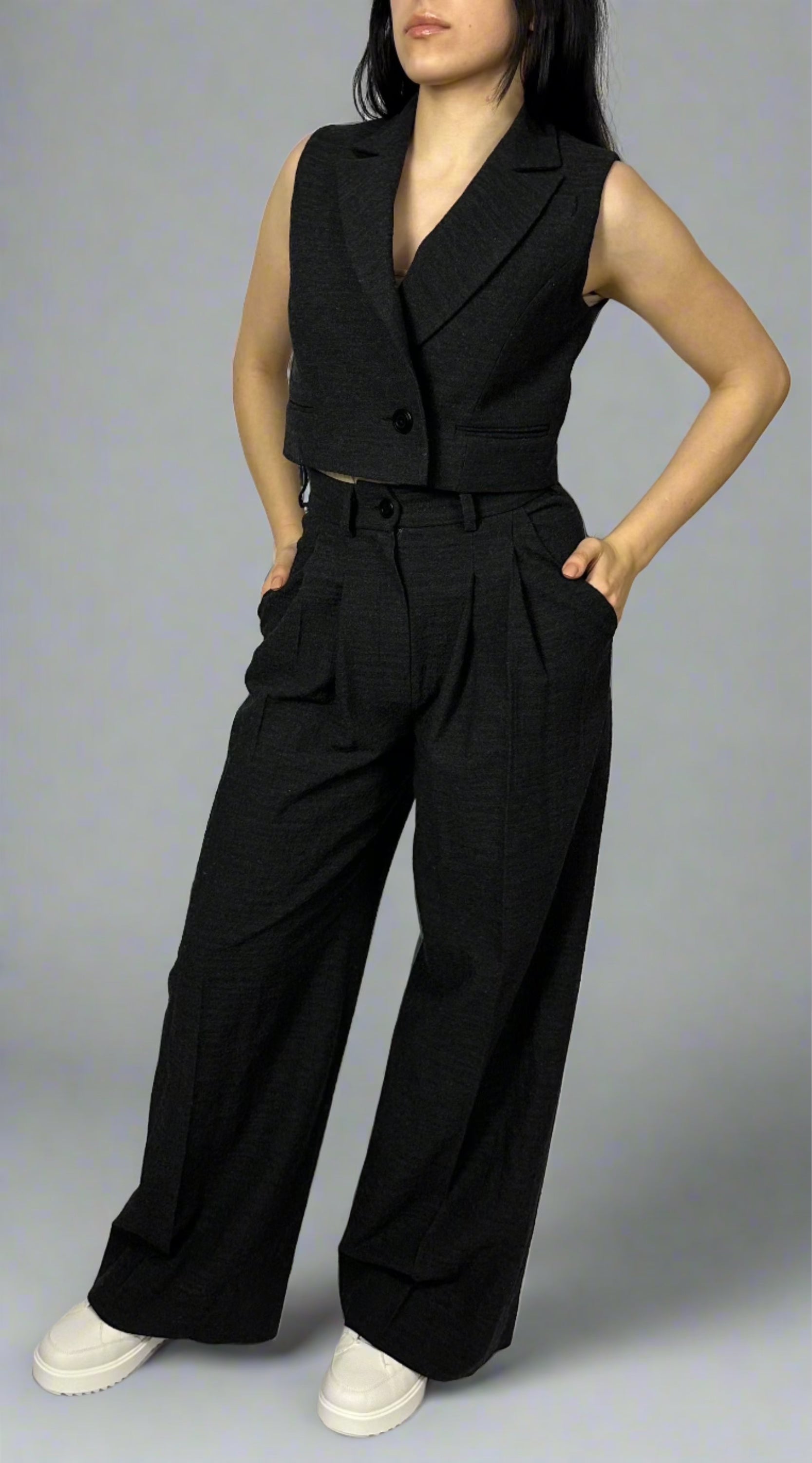 Model wearing Sartorial Flair’s black waistcoat with a single button and matching high-waisted wide-leg trousers. The ensemble is styled with white trainers for a smart casual look, showcasing the versatility of Sartorial Flair suits, suitable for both formal wear and stylish casual outfits.