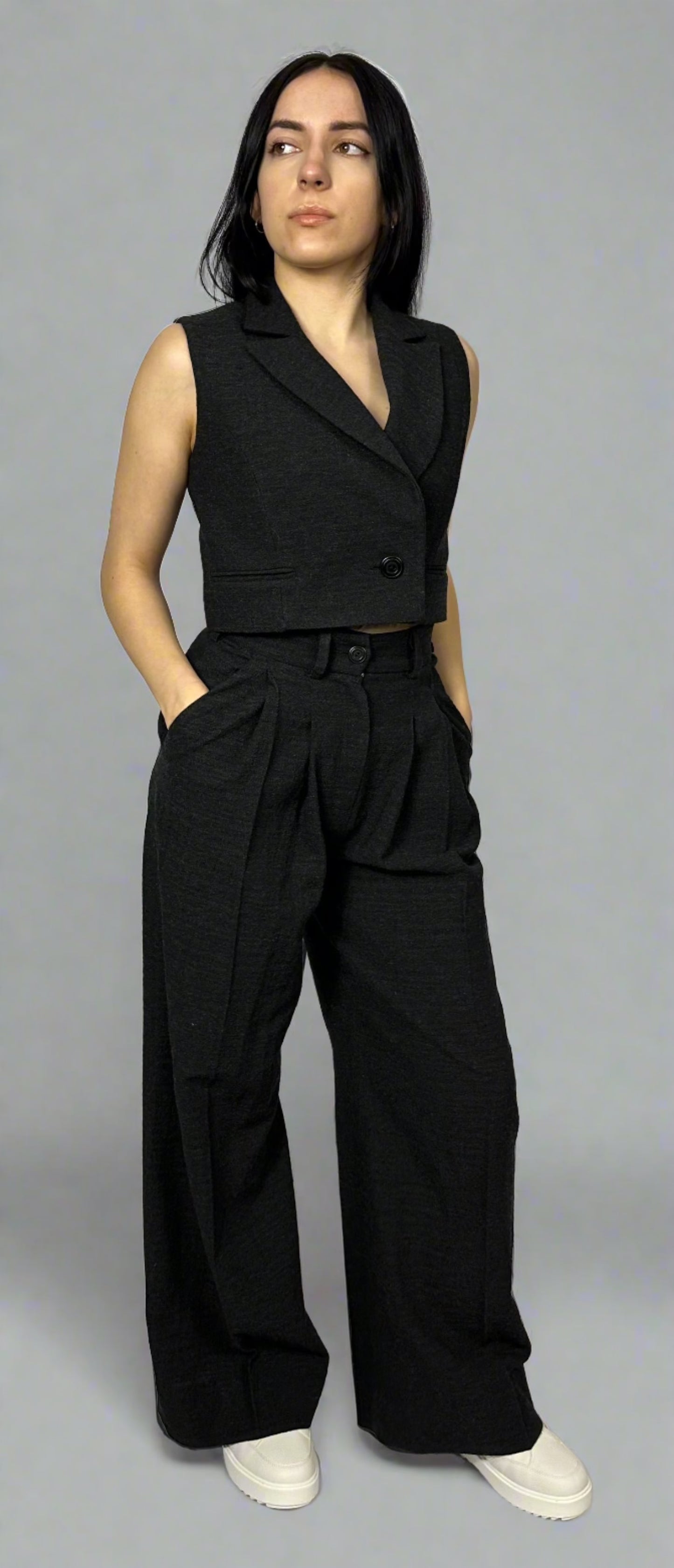 Model showcasing Sartorial Flair’s black waistcoat paired with wide-leg trousers. The waistcoat features a sharp, tailored fit with a single-button closure, while the high-waisted trousers have a pleated front, creating a chic and contemporary look. Perfect for professional settings or elegant evenings, this ensemble epitomizes modern sophistication.