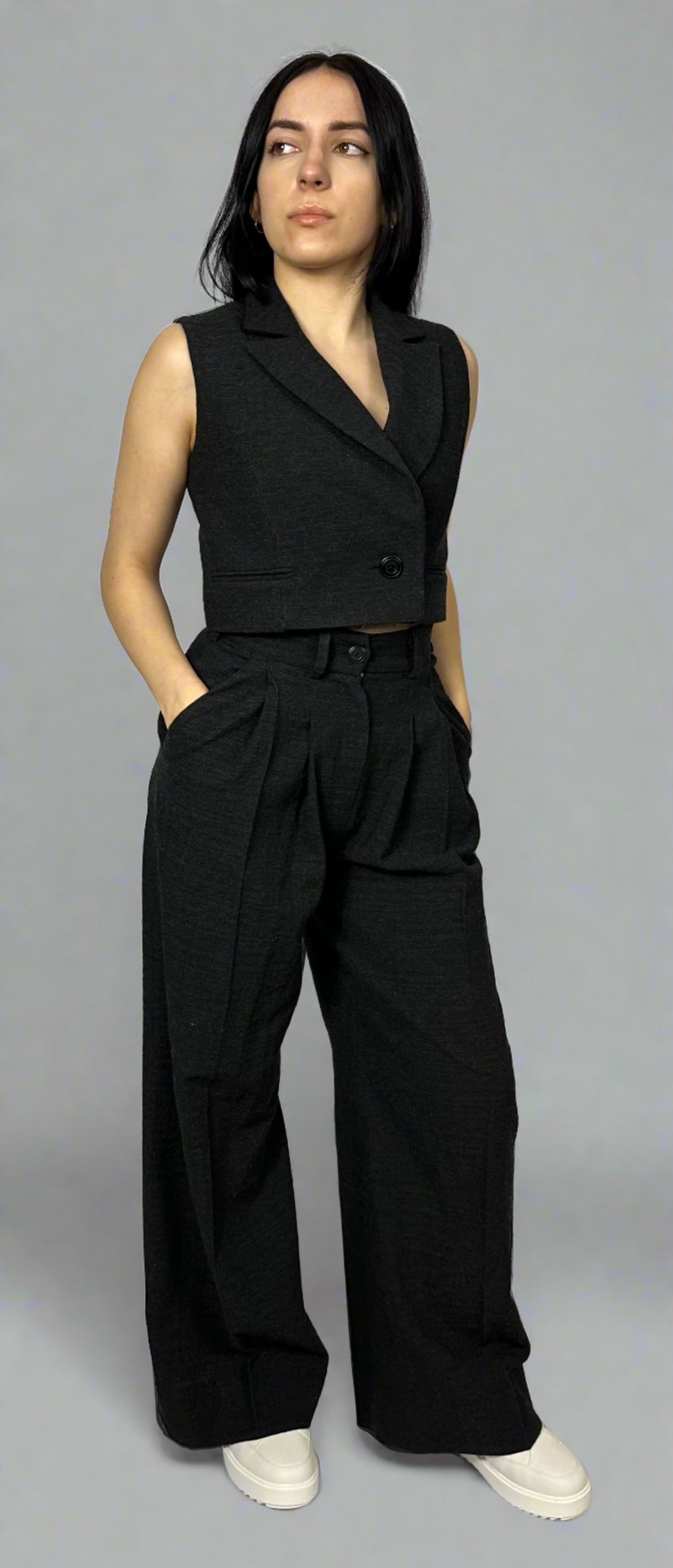 Model showcasing Sartorial Flair’s black waistcoat paired with wide-leg trousers. The waistcoat features a sharp, tailored fit with a single-button closure, while the high-waisted trousers have a pleated front, creating a chic and contemporary look. Perfect for professional settings or elegant evenings, this ensemble epitomizes modern sophistication.