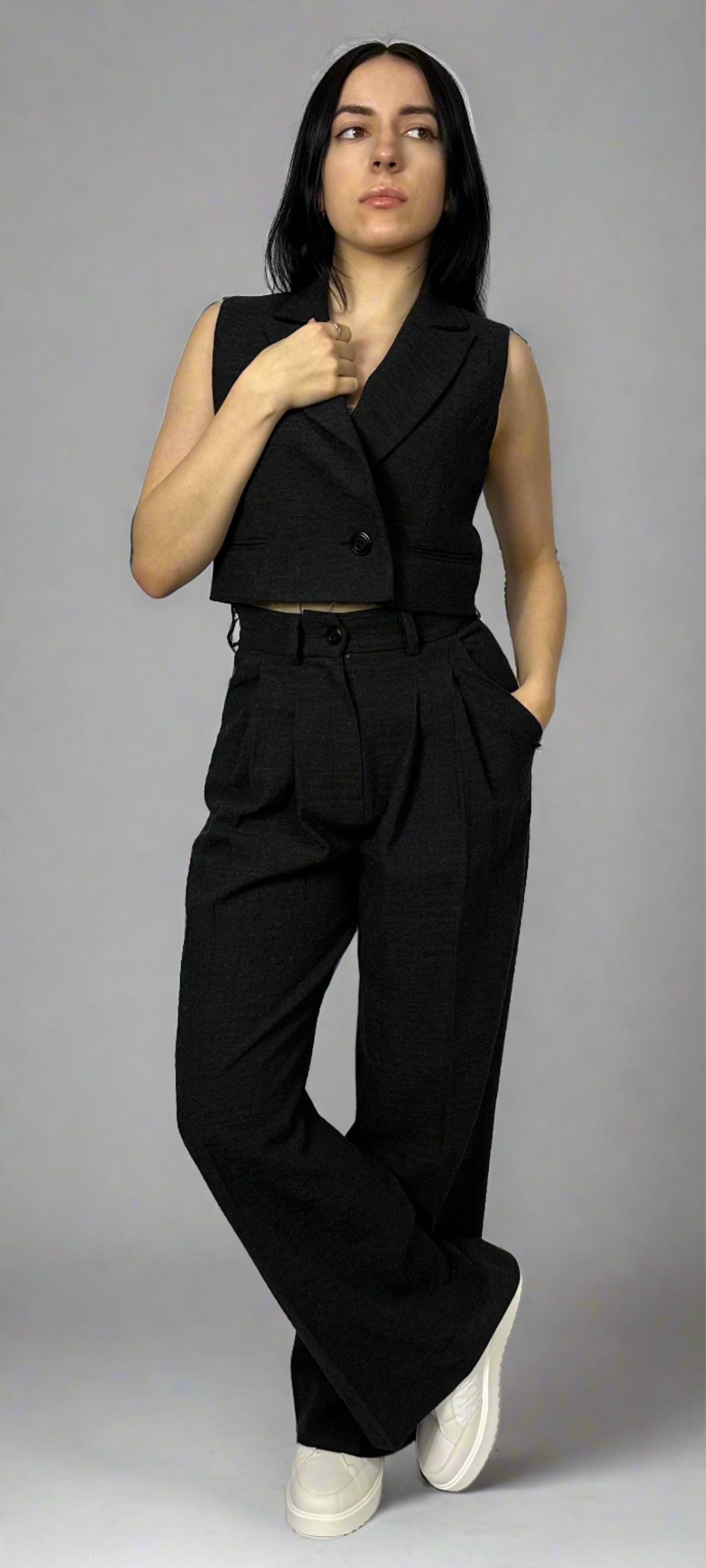 Model showcasing Sartorial Flair’s black waistcoat paired with matching wide-leg trousers. The waistcoat features a single-button design with a tailored fit, while the high-waisted trousers offer a pleated front and a comfortable wide-leg silhouette. This stylish ensemble by Sartorial Flair highlights modern sophistication, perfect for professional and formal settings.