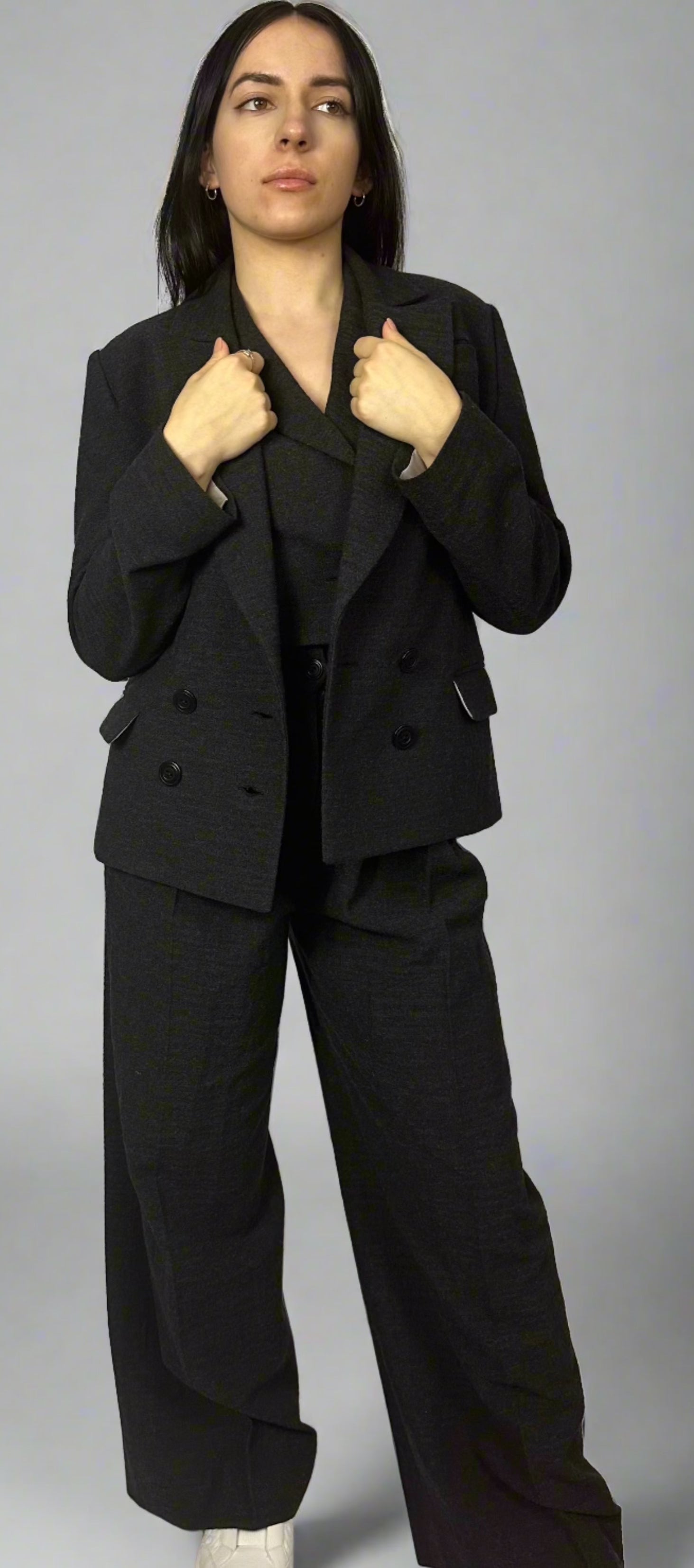 Model showcasing Sartorial Flair’s black double-breasted blazer paired with matching wide-leg trousers. The outfit features a sophisticated blazer with a classic lapel design and double-button closure, styled with a coordinated vest underneath. This look exemplifies professional elegance, perfect for formal or business settings, embodying Sartorial Flair’s modern yet timeless fashion approach.