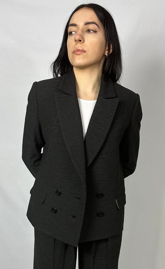 Model wearing Sartorial Flair’s black double-breasted blazer paired with matching wide-leg trousers. The tailored blazer features a classic lapel design and a double-button closure, exuding sophistication and elegance. This ensemble is ideal for professional or formal occasions, showcasing contemporary fashion with a timeless appeal.