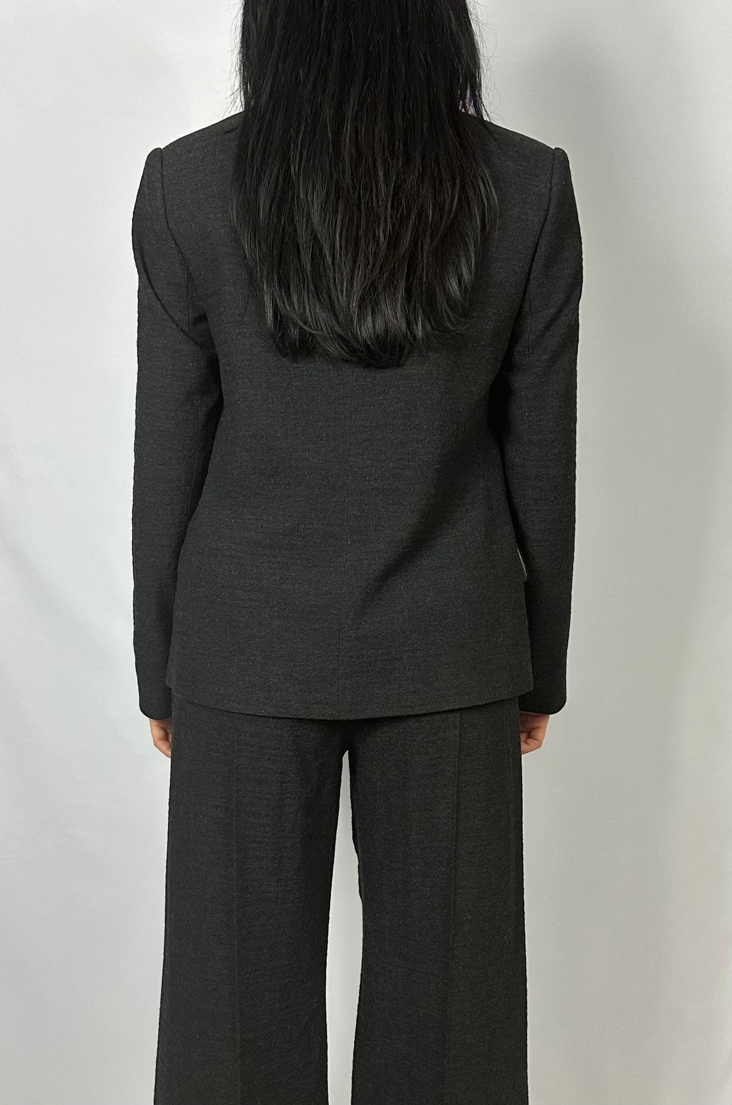 Rear view of a model wearing Sartorial Flair’s black double-breasted blazer paired with matching wide-leg trousers. The blazer, featuring a tailored fit, complements the trousers’ elegant drape, showcasing the professional and sophisticated style of Sartorial Flair. This outfit is ideal for formal business settings, embodying contemporary and timeless fashion.