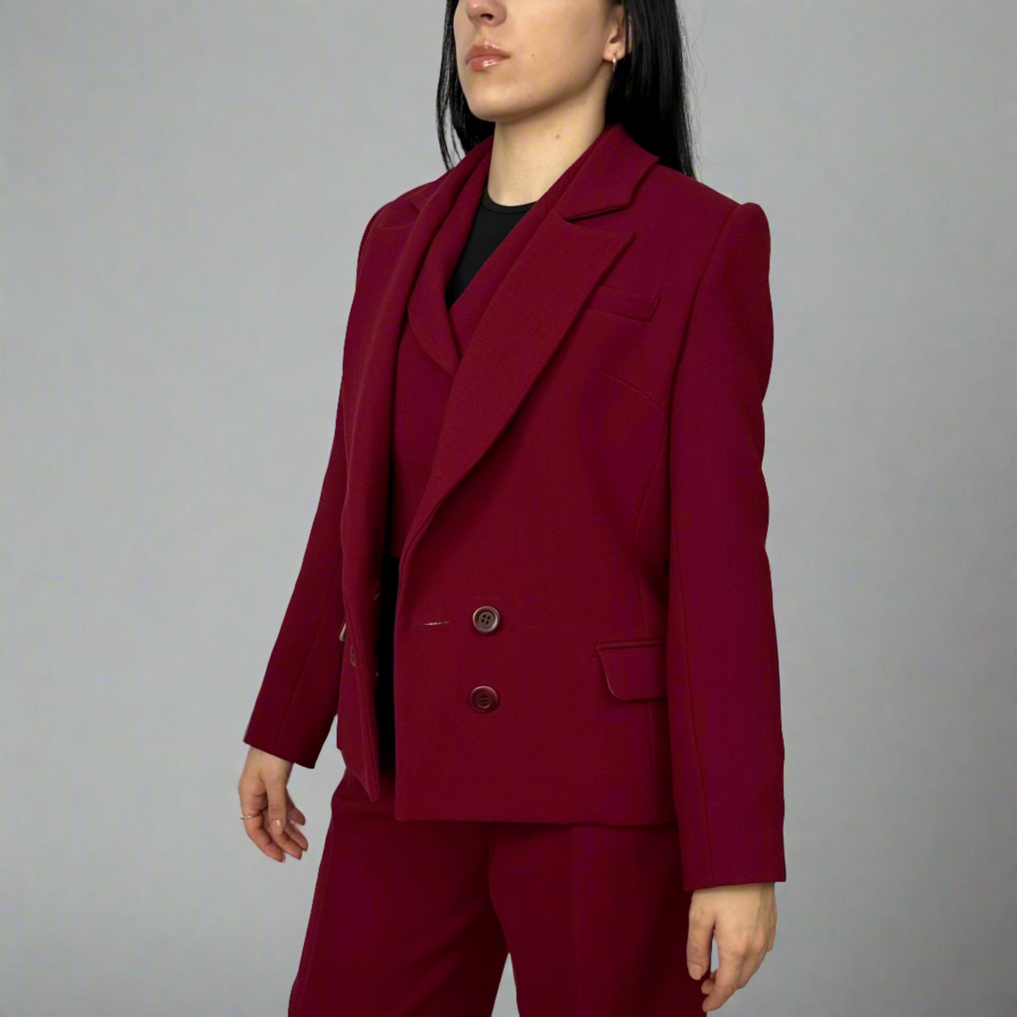 Stylish woman in a luxurious deep red Zoe suit featuring a modern blazer with wide lapels, matching trousers, and an elegant inner black top, showcasing Sartorial Flair’s commitment to sophisticated, sustainable fashion.